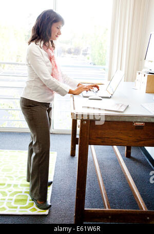 Imprenditrice lavorando in piedi alla sua scrivania in ufficio Foto Stock