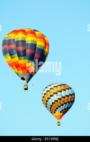 Una coppia di colorate mongolfiere in volo con cielo blu dietro durante il Bristol Balloon Fiesta si tiene annualmente Foto Stock