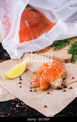 Pane con fette di salmone salato servita sulla carta da forno con limone, sale marino e peperoni. Foto Stock