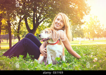 Gara di scena giovane e bella donna che abbraccia il suo cane beagle cucciolo di cane nel parco Foto Stock