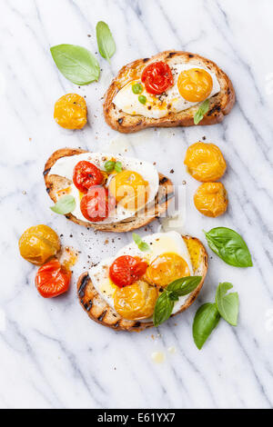 Bruschetta con pomodori arrosto e mozzarella su grigliate di crosta di pane su marmo bianco Foto Stock