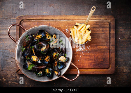 Le cozze in rame piatto di cottura e patatine fritte su scuro dello sfondo in legno Foto Stock