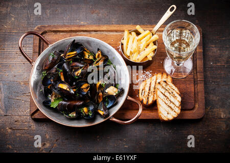 Le cozze in rame piatto di cottura e patatine fritte su scuro dello sfondo in legno Foto Stock