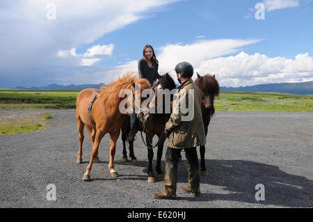 Turisti in visita in Islanda ottenendo la possibilità di cavalcare un pony Icelanic con un allevatore locale. Foto Stock