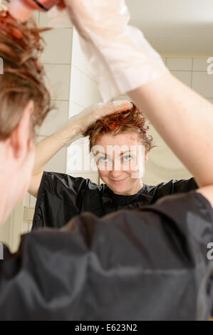 Caucasian donna con capelli corti morire i suoi capelli rosso nella parte anteriore dello specchio nel suo proprio bagno. Foto Stock