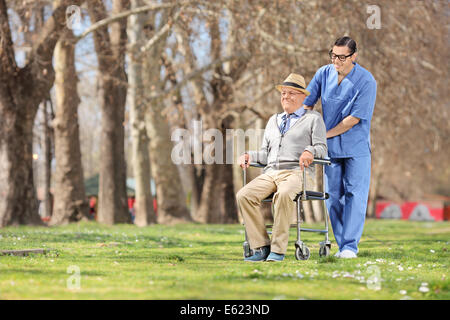 Infermiere spingendo un senior in sedia a rotelle all'aperto in una giornata di sole Foto Stock