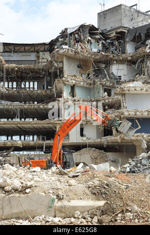 Un edificio a sei piani in cemento armato edificio ufficio in lettura è demolita utilizzando idraulico, escavatori cingolati Foto Stock