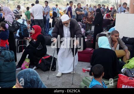 Rafah nella striscia di Gaza, Territori palestinesi. 12 Ago, 2014. Un uomo palestinese, sperando di attraversare in Egitto, siede su valigie come egli attende con gli altri al valico di Rafah tra Egitto meridionale e la striscia di Gaza il 12 agosto 2014. Sotto il presidente egiziano Abdel Fattah al-Sisi, Cairo ha fissato le chiusure sulla frontiera Gaza, aumentando la pressione economica su Hamas da un lungo assedio israeliano. I colloqui alla fine di un mese una lunga guerra tra Israele e militanti islamici a Gaza non hanno compiuto alcun progresso finora, un funzionario israeliano ha detto martedì, come settantadue ore di cessate il fuoco in frantumi enclav palestinese Foto Stock