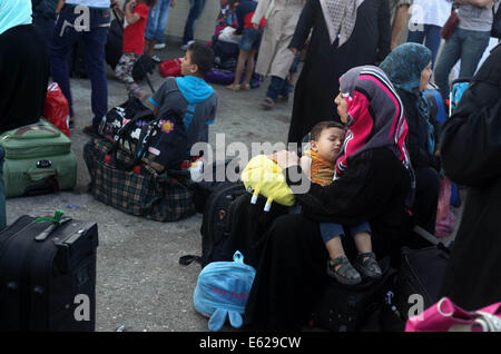 Rafah nella striscia di Gaza, Territori palestinesi. 12 Ago, 2014. Una donna Palestinese, sperando di attraversare in Egitto, mantiene il suo figlio in attesa con gli altri al valico di Rafah tra Egitto meridionale e la striscia di Gaza il 12 agosto 2014. Sotto il presidente egiziano Abdel Fattah al-Sisi, Cairo ha fissato le chiusure sulla frontiera Gaza, aumentando la pressione economica su Hamas da un lungo assedio israeliano. I colloqui alla fine di un mese una lunga guerra tra Israele e militanti islamici a Gaza non hanno compiuto alcun progresso finora, un funzionario israeliano ha detto martedì, come settantadue ore di cessate il fuoco in frantumi enclave palestinese Foto Stock