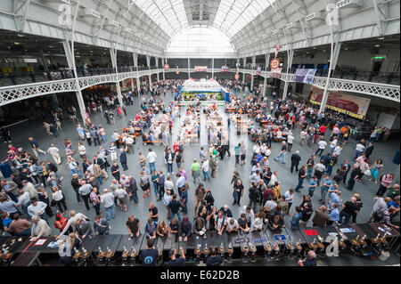 Olympia Exhibition Centre di Londra, Regno Unito. Il 12 agosto 2014. Il Great British Beer Festival ha iniziato il suo 5 giorno stint presso il centro espositivo di Olympia nel West London. Il festival organizzato dalla campagna per Real Ale (CAMRA), ha lanciato un appello all'azione il primo giorno che spera di vedere 55.000 agli spettatori del festival lobbying loro MP come il pub nel Regno Unito il tasso di chiusura aumenta a un valore stimato di 31 a settimana. Nella foto: una vista in elevato di Olympia e gli scommettitori godendo il Great British Beer Festival. Credito: Lee Thomas/Alamy Live News Foto Stock