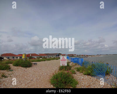 Pagham, West Sussex, Regno Unito. 12 agosto 2014. Erosione costiera prosegue lungo la costa sud, accelerata da recenti tempeste unseasonal. I bungalow sulla spiaggia a Pagham sono ora vicino al mare di avanzamento. Sono stati compiuti sforzi da Adur consiglio del distretto per proteggere le proprietà, autocarri evidenti oggi il ribaltamento di rocce di grandi dimensioni sulla ghiaia. Alcuni locali sono a dire che è troppo poco e troppo tardi e credo che a meno che la grande spiedo costruire è violato di nuovo come era in passato, ulteriore erosione è inevitabile. Credito: David Burr/Alamy Live News Foto Stock