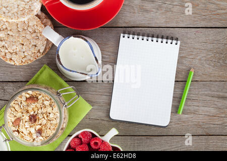 Salutare prima colazione con muesli, frutti di bosco e latte. Vista da sopra il tavolo in legno con il blocco note per lo spazio di copia Foto Stock