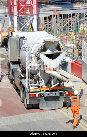 Marshall di traffico dirigere un camionista invertendo ready mix concrete camion da cantiere su una strada trafficata utilizzando degli specchietti retrovisori Foto Stock