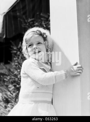 1930s sorridente bambina indossa un maglione Berretto in maglia di mantenere il portico pilastro BANNISTER Foto Stock