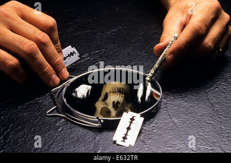 Anni Novanta mani tenendo la lama di un rasoio e un ARROTOLATO $20.00 BILL OLTRE LO SPECCHIO COPERTO CON LA COCAINA con la riflessione di un cranio Foto Stock