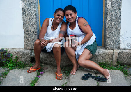 Due donne amichevole seduti sulla soglia di casa, Paraty, Stato di Rio de Janeiro, Brasile Foto Stock