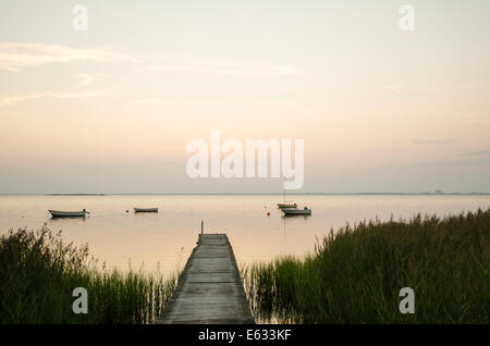 Un vecchio pontile in legno ancorato con piccole imbarcazioni in una baia tranquilla a Twilight time Foto Stock