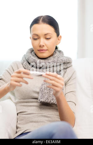Ill donna con influenza a casa guardando il termometro Foto Stock