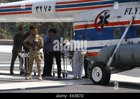 Il Cairo, Egitto. 13 Ago, 2014. Un poliziotto sta di guardia nei pressi di un elicottero mentre medical lavoratori portano ex presidente egiziano Hosni Mubarak fuori da un elicottero per il suo ospedale a Il Cairo, Egitto, 13 Agosto, 2014. Egyptian ex presidente egiziano Hosni Mubarak ha detto Mercoledì in tribunale che non ha dato alcun ordine di uccidere i manifestanti durante il 2011 insurrezione popolare contro il suo lungo tempo regola e statali Nile TV segnalati. Credito: Ahmed Gomaa/Xinhua/Alamy Live News Foto Stock