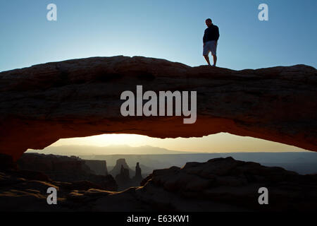 Persona sulla Mesa Arch e sunrise oltre La Sal Mountains, il Parco Nazionale di Canyonlands, Utah, Stati Uniti d'America Foto Stock