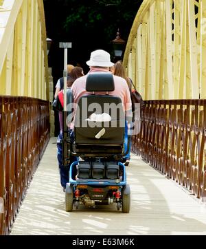 Un uomo a cavallo di uno scooter di mobilità attraverso il ponte del Giubileo matlock bath derbyshire England Regno Unito Foto Stock