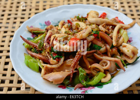 Primo piano della stir-calamari fritti e basilico su piastra bianca e bambù di sfocatura dello sfondo cestello ; messa a fuoco selettiva con blur backgroun Foto Stock