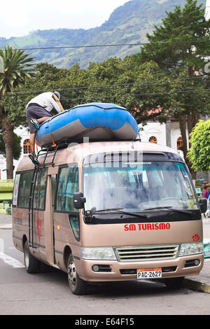 BANOS, ECUADOR - 25 febbraio 2014: persona non identificata la scalata verso il basso un minibus con una barca di gomma sul portapacchi del tetto Foto Stock