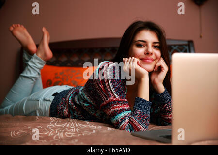 Allegra donna sdraiata sul letto con il computer portatile Foto Stock