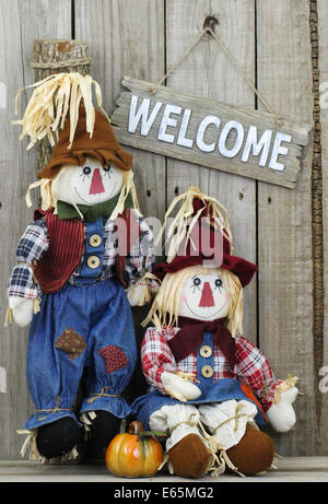 Un ragazzo e una ragazza scarecrows con zucca e rustici in legno segno di benvenuto appeso sul weathered recinzione di legno Foto Stock