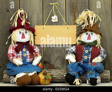 Un ragazzo e una ragazza seduta scarecrows sul log di zucca e vuoto segno di legno appeso alla recinzione rustico Foto Stock