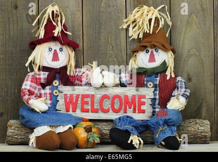 Un ragazzo e una ragazza seduta scarecrows sul log azienda weathered legno segno di benvenuto Foto Stock