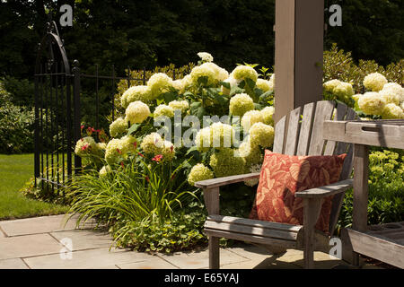 In estate i fiori sbocciano da una pergola di sole impostazione con una sedia Adirondack in Massachusetts Foto Stock