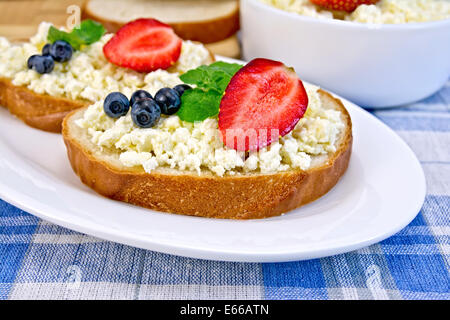 Fette di pane con crema di ricotta, menta, mirtilli e fragole, una ciotola di formaggio, pane su una scheda su uno sfondo Foto Stock