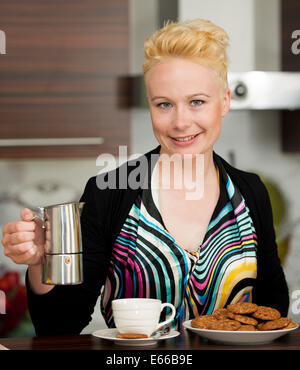 Giovane e bella caucasian donna bionda la cottura di caffè espresso in accogliente cucina Foto Stock