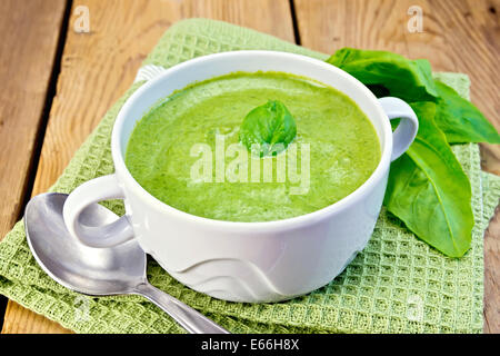 Zuppa verde purea in una ciotola con il verde di spinaci in foglia, cucchiaio su un tovagliolo sullo sfondo delle tavole di legno Foto Stock