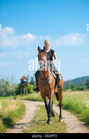 Giovane e bella donna bionda in sella ad un cavallo in un agriturismo Foto Stock