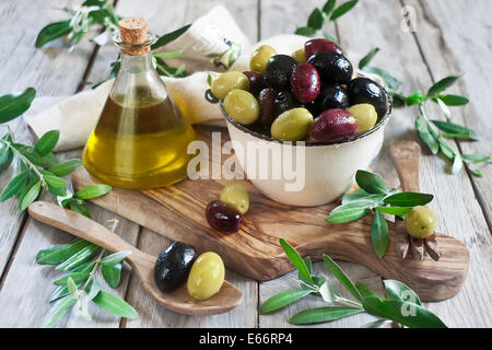 Misto di olive marinate (verde, nero e viola) nel vaso di ceramica e il cucchiaio di legno con bottiglia di olio d'oliva. Messa a fuoco selettiva. Foto Stock