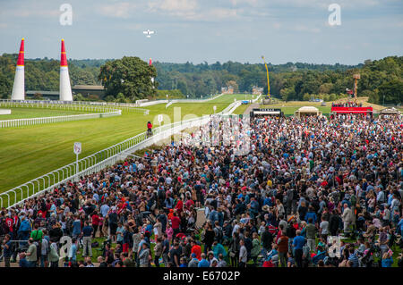 Il round britannico della Red Bull Air Race si terrà presso il pittoresco ippodromo di Ascot. Grande folla di pubblico che riempie le aree degli spettatori, con l'aereo che si allontana dal circuito Foto Stock