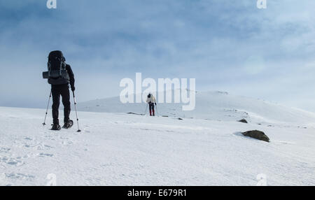 Due uomini con zaini pesanti con le racchette da neve attraverso un inverno paesaggio di montagna. Huldraheimen, Gausdal vestfjell, Norvegia Foto Stock