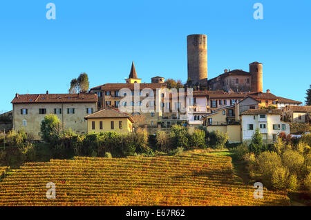 Vigneti di colore giallo e il piccolo borgo medievale sulla collina in autunno in Piemonte, Italia settentrionale. Foto Stock