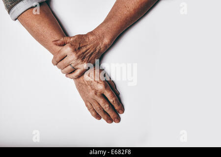 Vista dall'alto di una donna anziana con le mani in mano in appoggio su uno sfondo grigio. Rilassata vecchie mani femminili insieme. Foto Stock