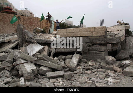 Hebron, West Bank, Territorio palestinese. 18 Agosto, 2014. Ragazzi palestinesi tenere le bandiere nazionali come la loro posizione sulle macerie di un Hossam Al-Qawasmi house è distrutto dall esercito israeliano, in Cisgiordania città di Hebron il 18 agosto 2014. Le Forze di Difesa Israeliane demolito le case di due sospetti in giugno il rapimento e l uccisione di tre ragazzi israeliani tarda notte di lunedì, mentre inoltre tenuta alla residenza di un terzo credito sospetto: Mamoun Wazwaz APA/images/ZUMA filo/Alamy Live News Foto Stock