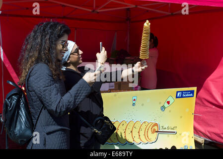 Battersea Park, Food Festival. Londra REGNO UNITO. 17 Agosto 2014 Due donne fotografia il loro moto vorticoso di patate sui loro telefoni intelligenti. Foto Stock