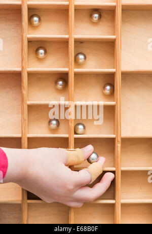 La mano del bambino di immissione di piccole sfere di acciaio in una scatola di legno con vani. Immagine concettuale di organizzazione, struttura e raccolta Foto Stock