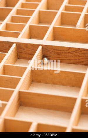 Piccola sfera di acciaio nella scatola di legno con scomparti vuoti. Immagine concettuale di solitudine, di solitudine e di rimanere intrappolati. Foto Stock