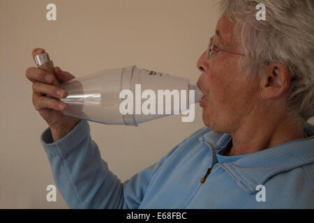 Anziana donna asmatica utilizzando un distanziatore Volumatic dispositivo per inalatore di steroidi Foto Stock