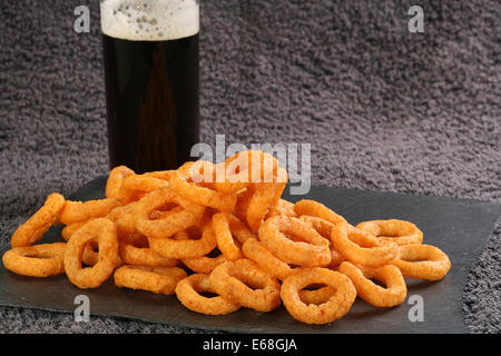 Pila di cipolla croccante aromatizzato spuntini wit un bicchiere di birra Foto Stock