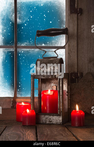 Quattro masterizzazione rosso Natale candele con una vecchia lanterna di stagno - decorato in legno davanzale. Foto Stock