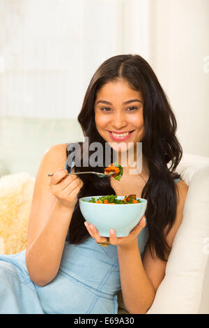 Donna ispanica insalata mangiare sul divano Foto Stock