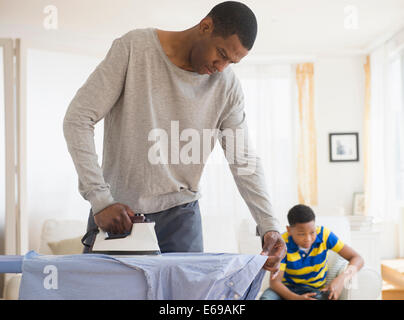 Padre la stiratura camicia mentre il figlio gioca giochi video Foto Stock